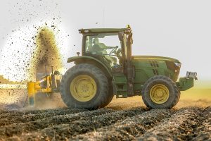 Side view of Dominator Vertical Rotary Ditcher in the field with green tractor