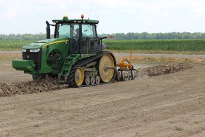Side view of the AMCO LJ6 Levee Plow in field with green tractor