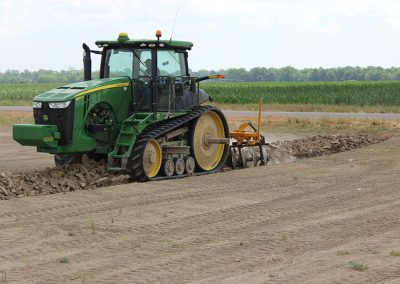 Side view of the AMCO LJ6 Levee Plow in field with green tractor