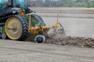 Side view of AMCO LJ6 Levee Plow in field with green tractor