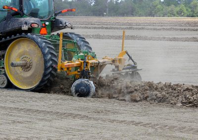 Side view of AMCO LJ6 Levee Plow in field with green tractor
