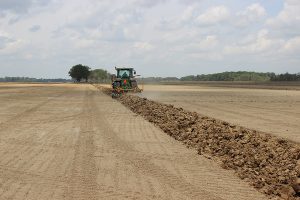 Full view of AMCO LJ6 Levee Plow in the field with a tractor