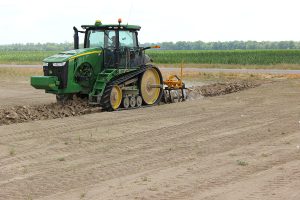 Side view of AMCO TJ3 Terracing Plow in field with green tractor
