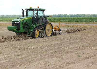 Side view of AMCO TJ3 Terracing Plow in field with green tractor