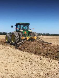 Full view of AMCO TJ3 Terracing Plow running in field with green tractor