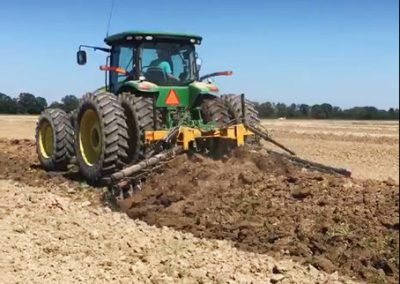 Full view of AMCO TJ3 Terracing Plow running in field with green tractor